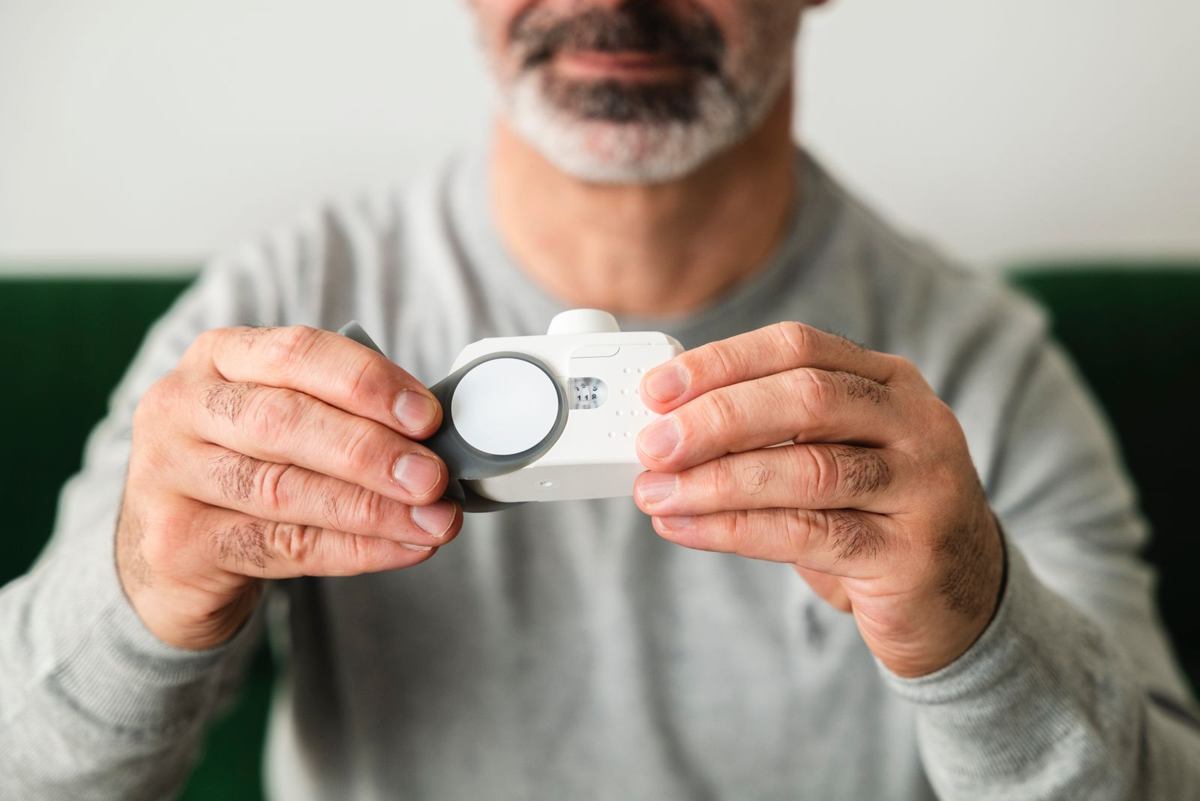 Close-up of a homeowner's hands holding a small handheld indoor air quality monitor, the kind of device used to check a home's air before and after mitigation