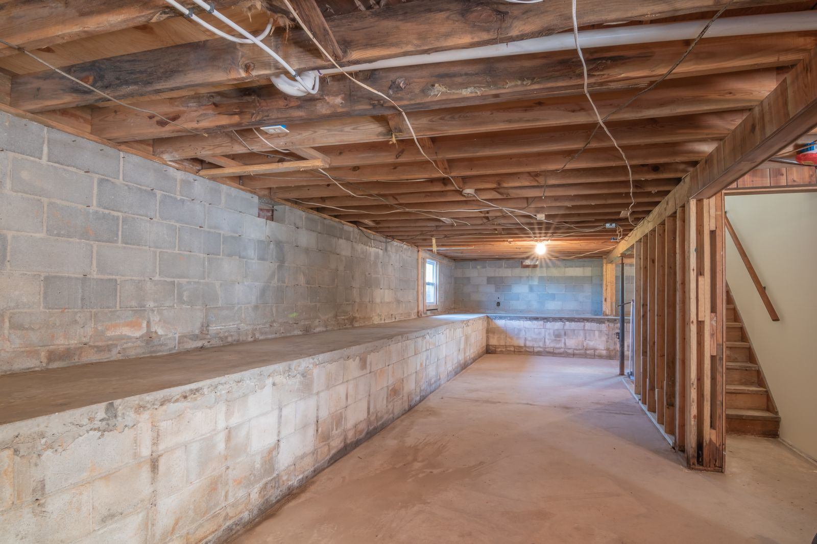 Unfinished basement with concrete block walls, exposed floor joists, and a bare concrete slab, the kind of space a sub-slab radon system is installed in